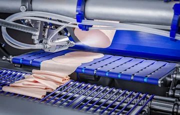 Sistema SprayTech che nebulizza un sottile strato di liquido sui salumi affettati presenti su un nastro trasportatore.